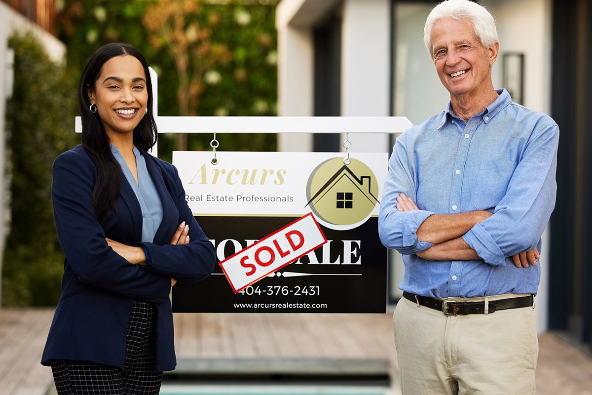 A real estate agent and a happy customer standing in front of a sold sign.