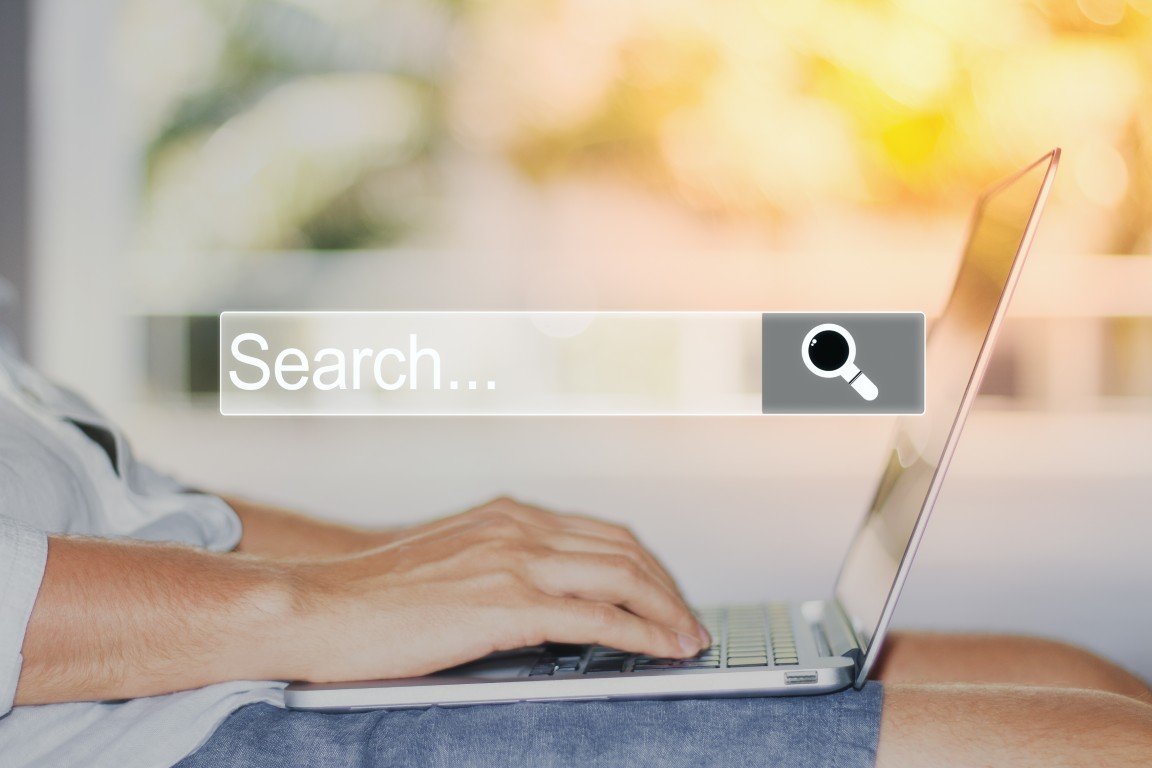A search bar graphic above a woman's hands on a laptop keyboard