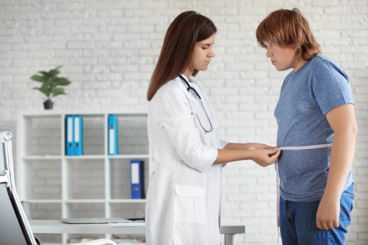 Female doctor in a white coat measures a man's waist with a tape in a clinic room.