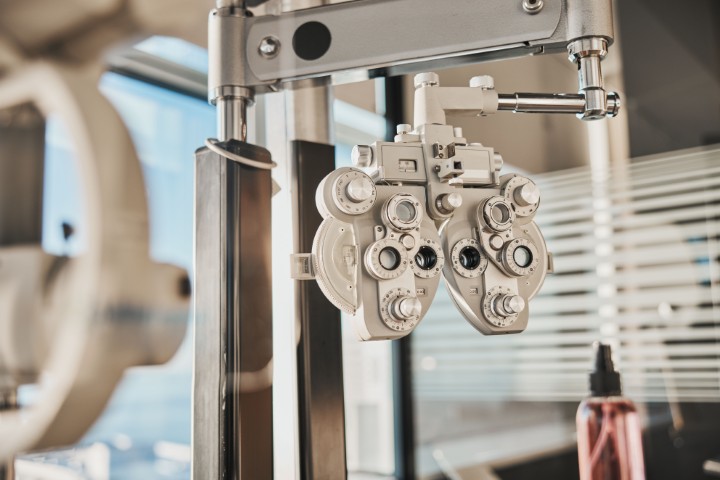 Phoropter used during an eye exam, hanging in front of a patient chair, ready to test vision refractivity.
